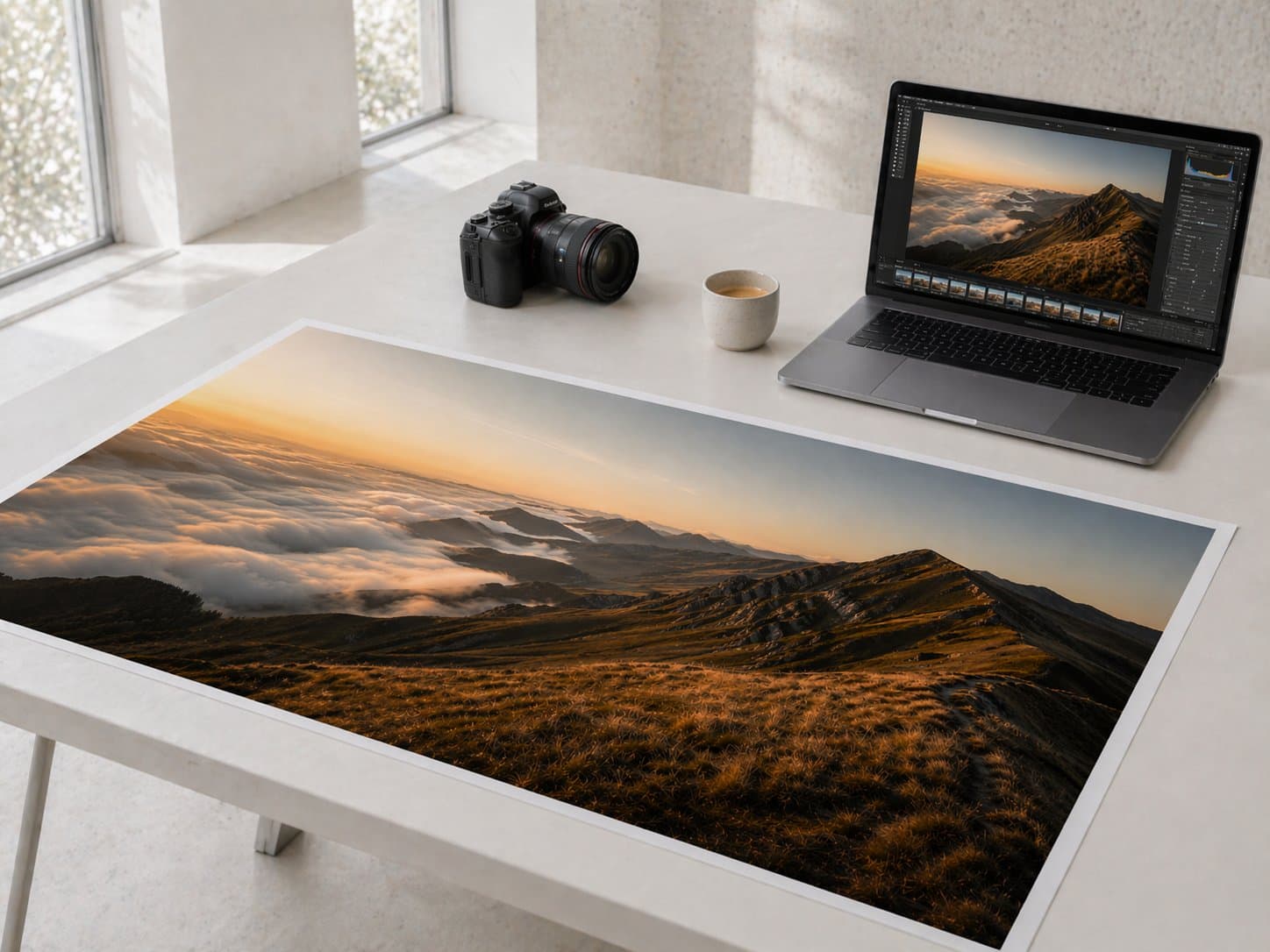 Photographer's workspace — a large print of the mountain landscape alongside a camera and laptop